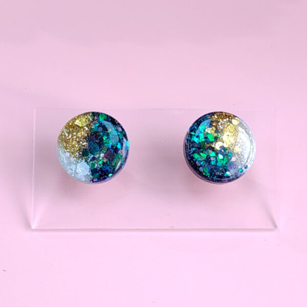 Add a celestial touch with the Night Sky Gems from Orellie. These stunning round stud earrings shimmer with a cosmic blend of glitter and hues, perfect for any occasion or everyday sparkle.