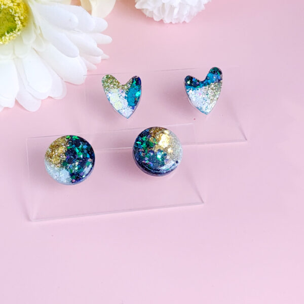 Add a touch of celestial charm with the Night Sky Sparkle Hearts from Orellie. These glittering heart-shaped stud earrings feature a cosmic mix of blues, greens, and golds, perfect for adding a hint of elegance to any outfit.