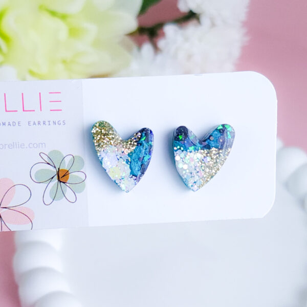 Add a touch of celestial charm with the Night Sky Sparkle Hearts from Orellie. These glittering heart-shaped stud earrings feature a cosmic mix of blues, greens, and golds, perfect for adding a hint of elegance to any outfit.