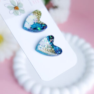 Add a touch of celestial charm with the Night Sky Sparkle Hearts from Orellie. These glittering heart-shaped stud earrings feature a cosmic mix of blues, greens, and golds, perfect for adding a hint of elegance to any outfit.