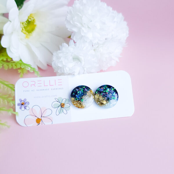 Add a celestial touch with the Night Sky Gems from Orellie. These stunning round stud earrings shimmer with a cosmic blend of glitter and hues, perfect for any occasion or everyday sparkle.