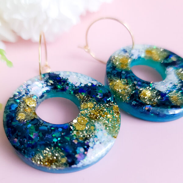 Embrace celestial elegance with the Night Sky Hoops from Orellie. These handmade glittering hoop earrings feature dazzling shades of deep blue, green, and gold, perfect for a bold statement look or a touch of nighttime magic.