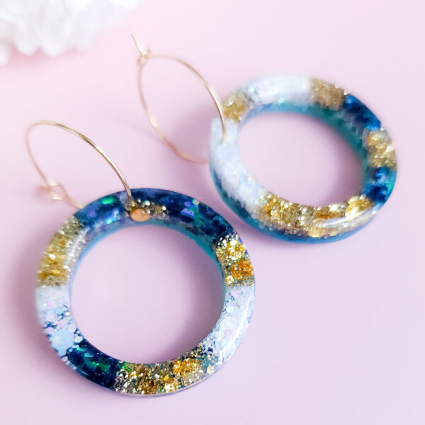 Embrace celestial beauty with Night Sky Orbit earrings from Orellie. Featuring glittering accents of gold and blue, these handmade hoops add elegance to every look, whether casual or formal.