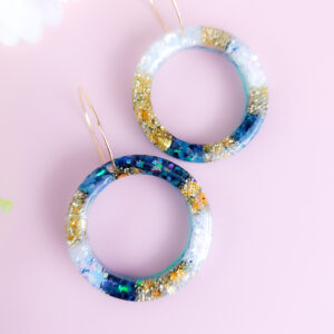 Embrace celestial beauty with Night Sky Orbit earrings from Orellie. Featuring glittering accents of gold and blue, these handmade hoops add elegance to every look, whether casual or formal.