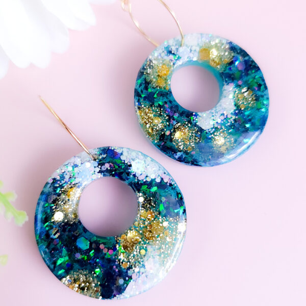 Embrace celestial elegance with the Night Sky Hoops from Orellie. These handmade glittering hoop earrings feature dazzling shades of deep blue, green, and gold, perfect for a bold statement look or a touch of nighttime magic.