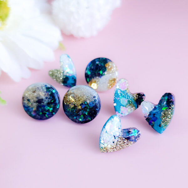 Add a celestial touch with the Night Sky Gems from Orellie. These stunning round stud earrings shimmer with a cosmic blend of glitter and hues, perfect for any occasion or everyday sparkle.