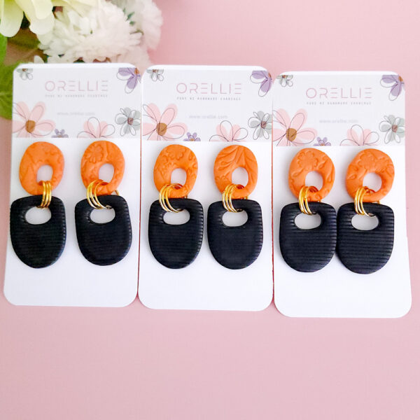 Elevate your style with the Twilight Loop earrings from Orellie. These handcrafted earrings feature a bold contrast of textured orange and black, complemented by golden accents, perfect for making a unique statement at any occasion.