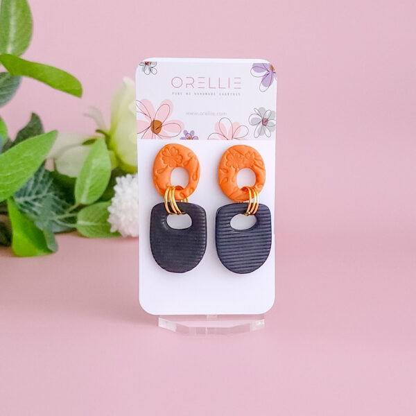 Elevate your style with the Twilight Loop earrings from Orellie. These handcrafted earrings feature a bold contrast of textured orange and black, complemented by golden accents, perfect for making a unique statement at any occasion.